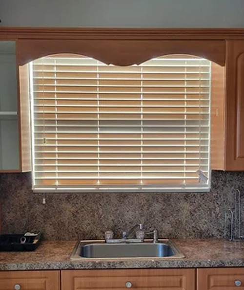 Faux wood blinds on a kitchen window above the sink