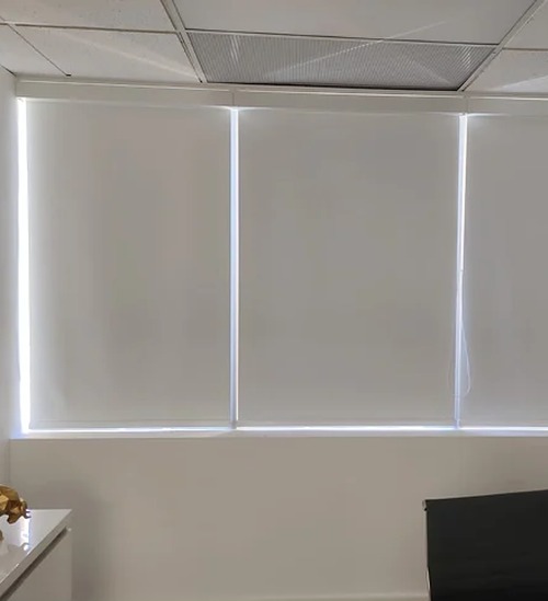 White roller shades on three windows with light around the edges