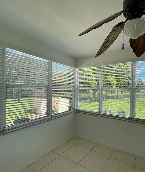 Horizontal blinds on windows in a bright sunroom with a ceiling fan